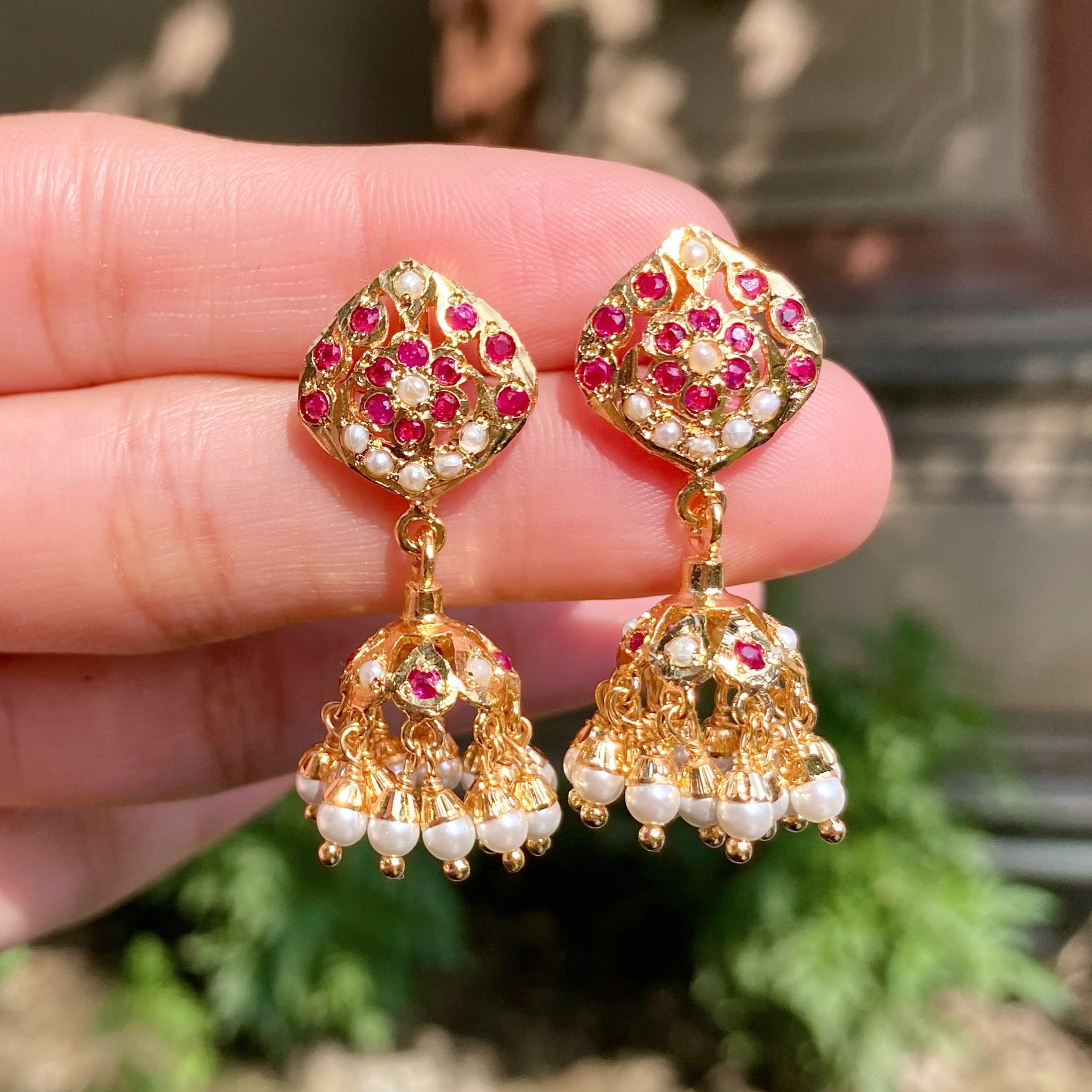 Gold earrings with red and white stones held between fingers against a blurred background