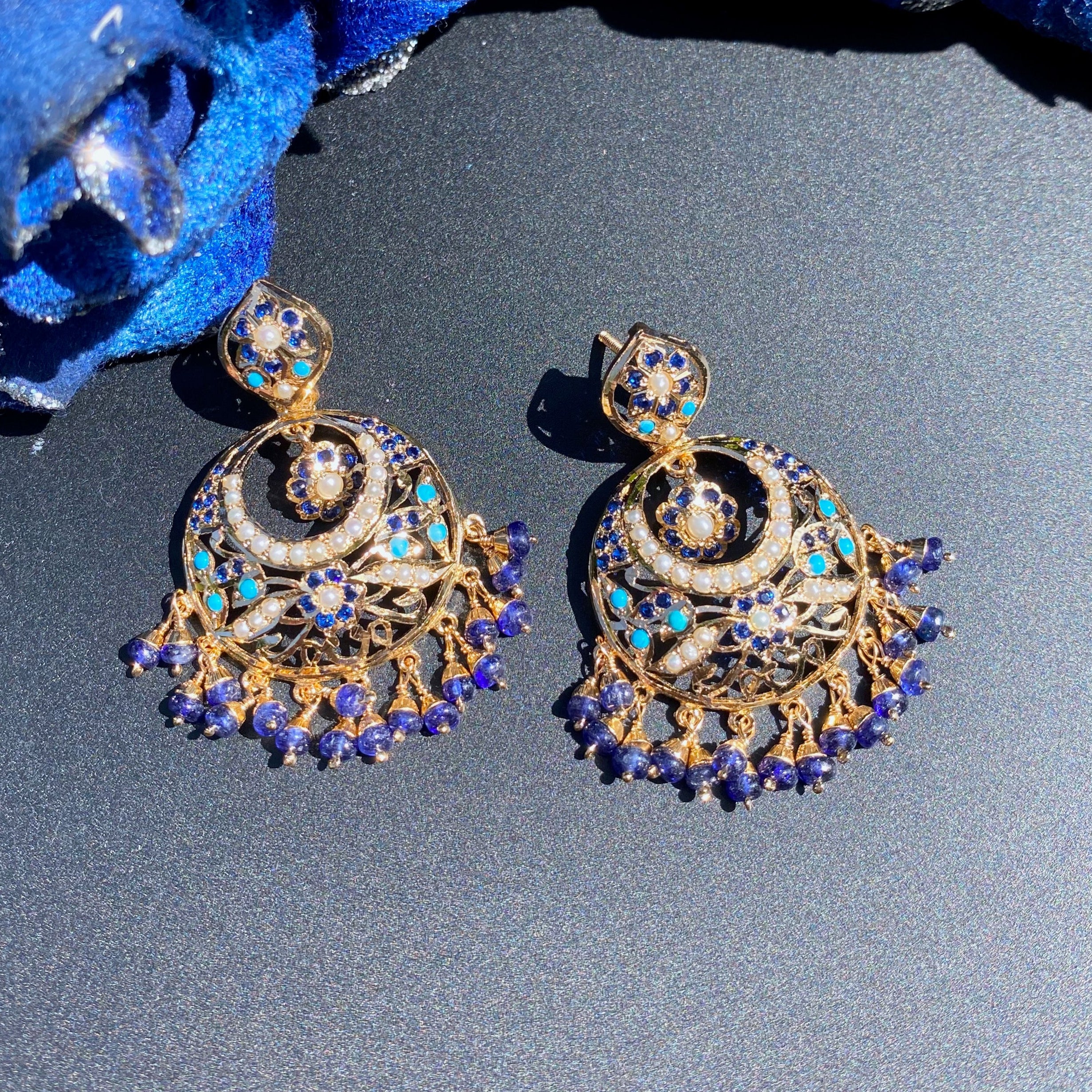 Gold and blue earrings on a dark surface with blue flowers in the background
