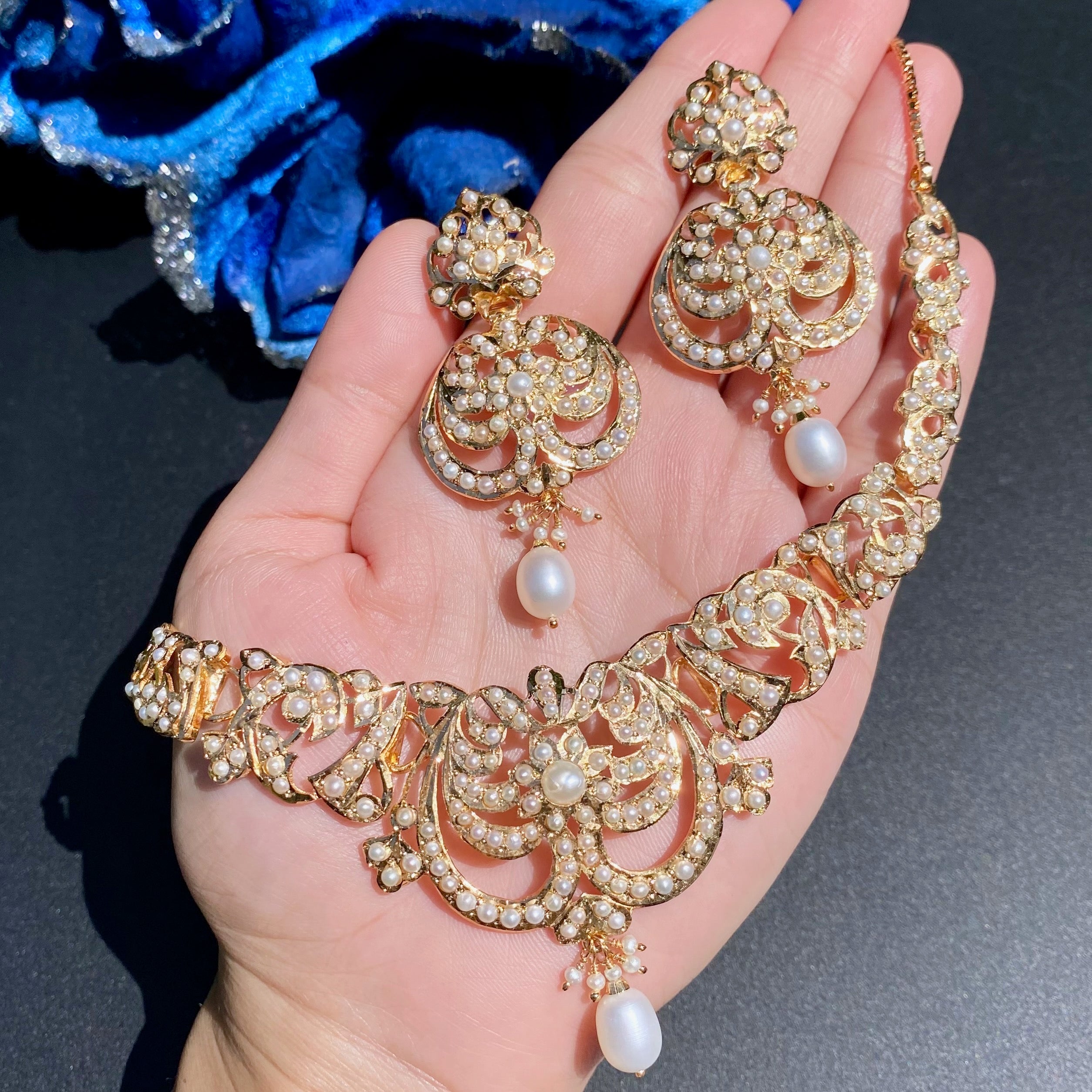 Ornate gold necklace with pearls held in a hand against a dark background