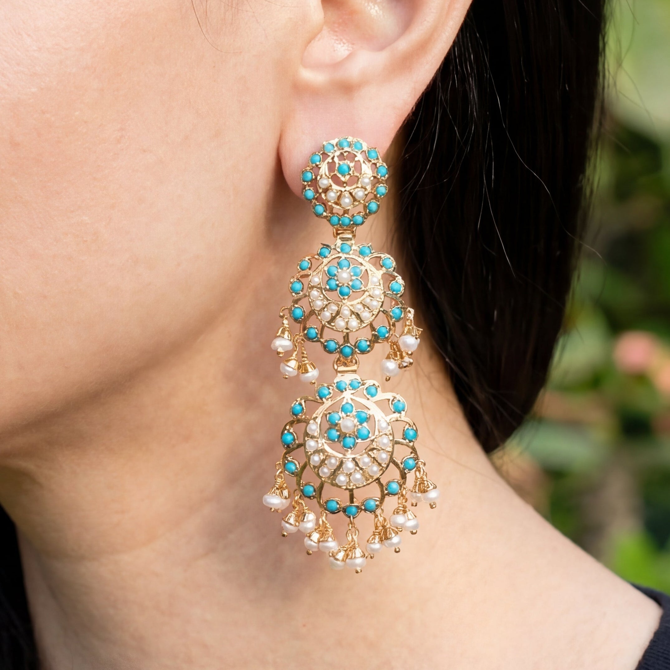 Woman wearing gold and turquoise earrings with a blurred green background