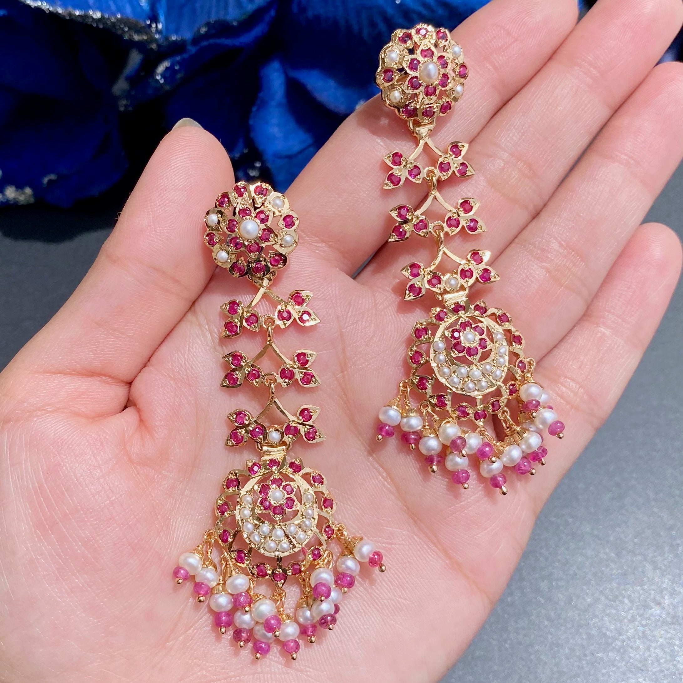 Gold earrings with pink and white stones on a hand