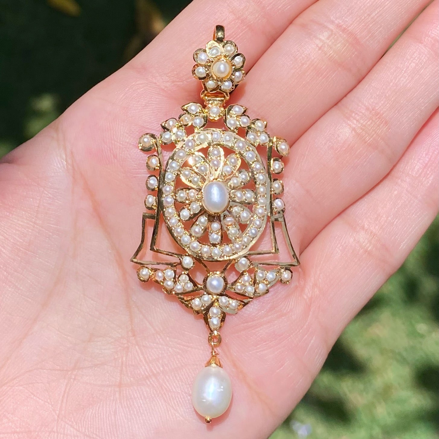 Decorative gold and pearl pendant held in a hand with a blurred green background