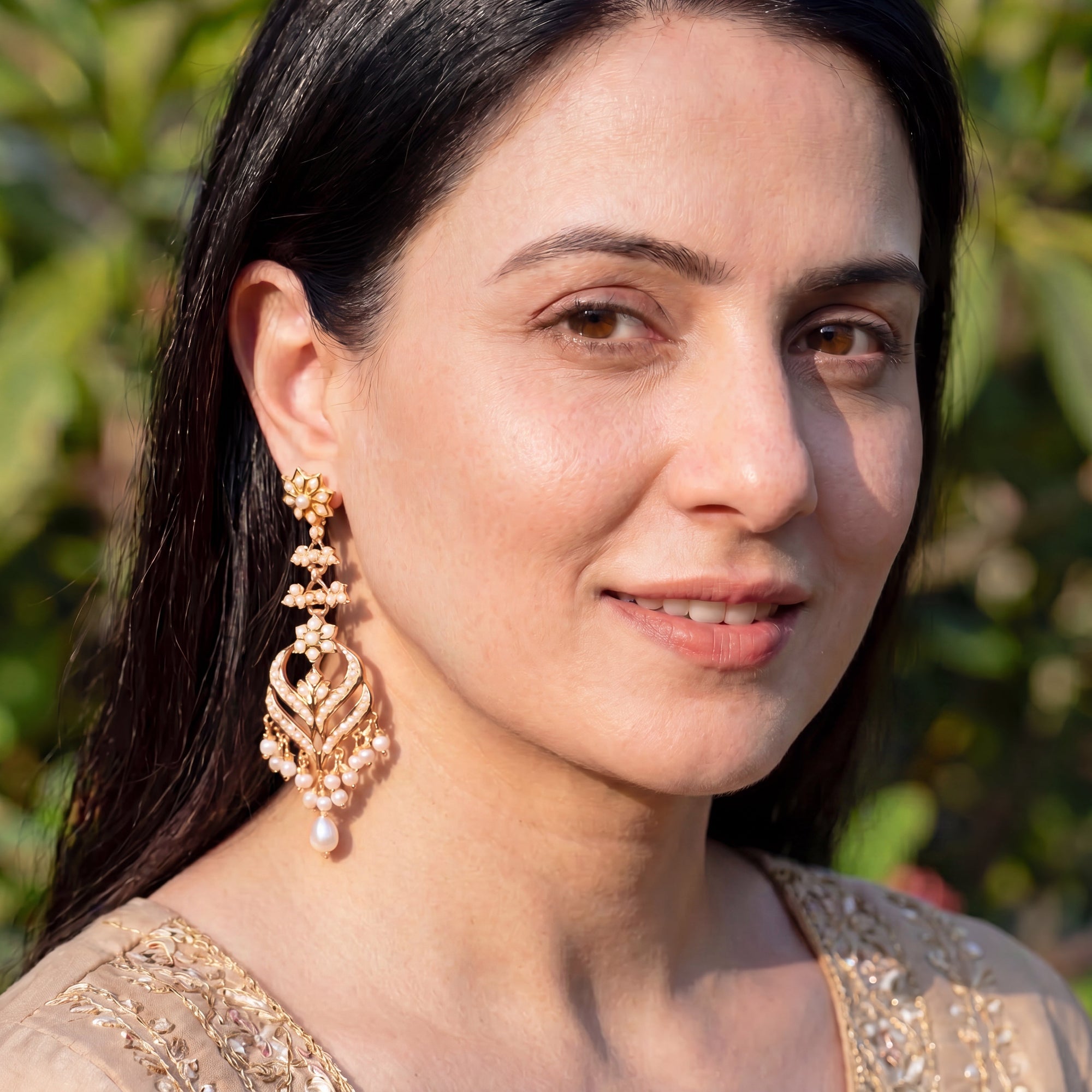 indian Woman wearing long gold and pearl earrings with a blurred green background