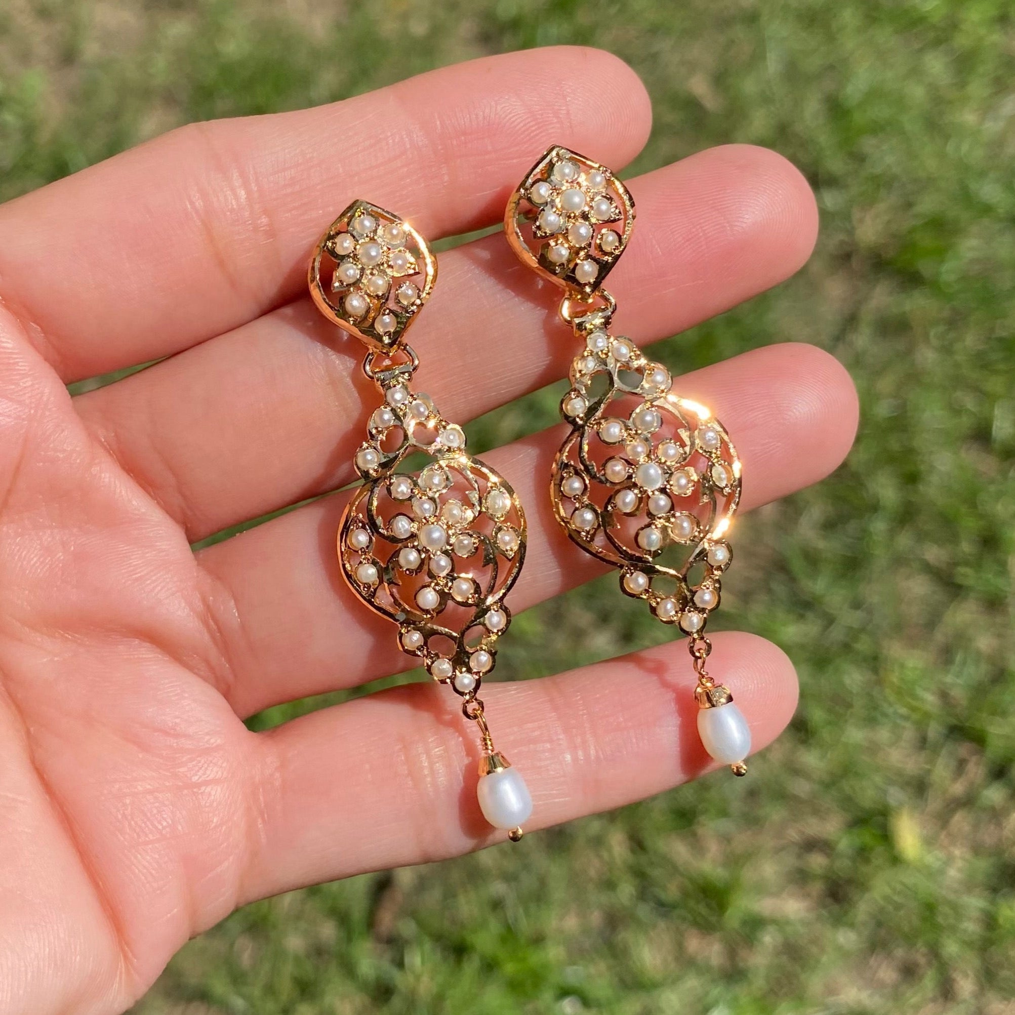 Rose gold earrings with pearl accents held in a hand against a grassy background