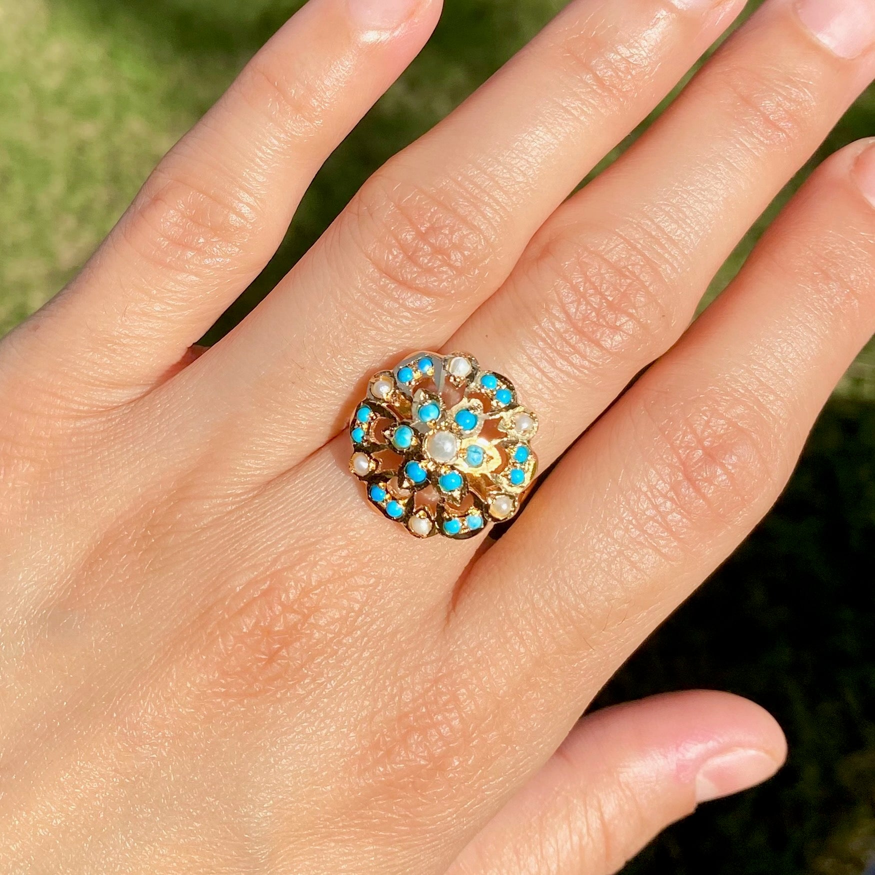 Close-up of a hand wearing a decorative ring with blue and gold stones against a blurred green background