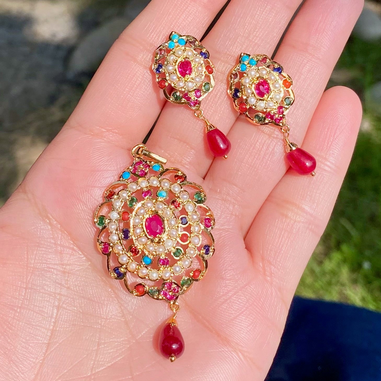 Colorful gemstone earrings held in a hand with a blurred natural background