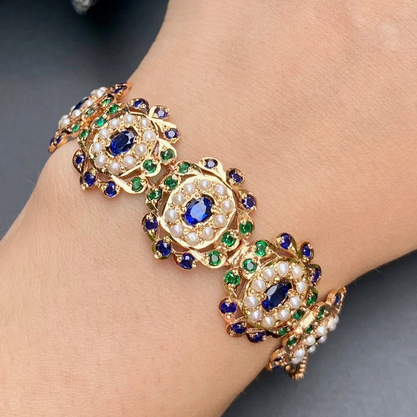 Gold bracelet with blue and green gemstones on a wrist against a dark background