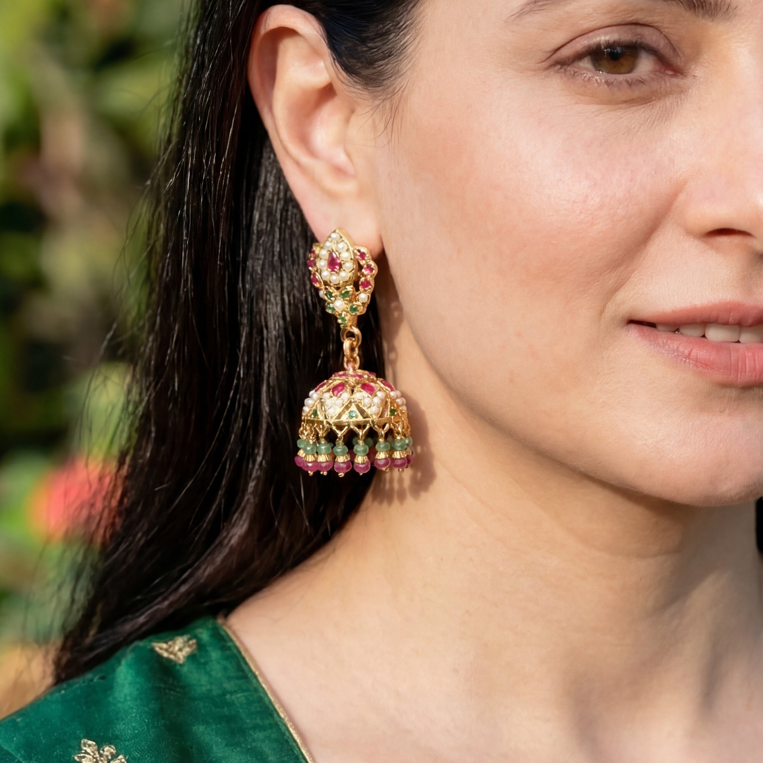Woman wearing traditional earrings with a green outfit against a blurred natural background