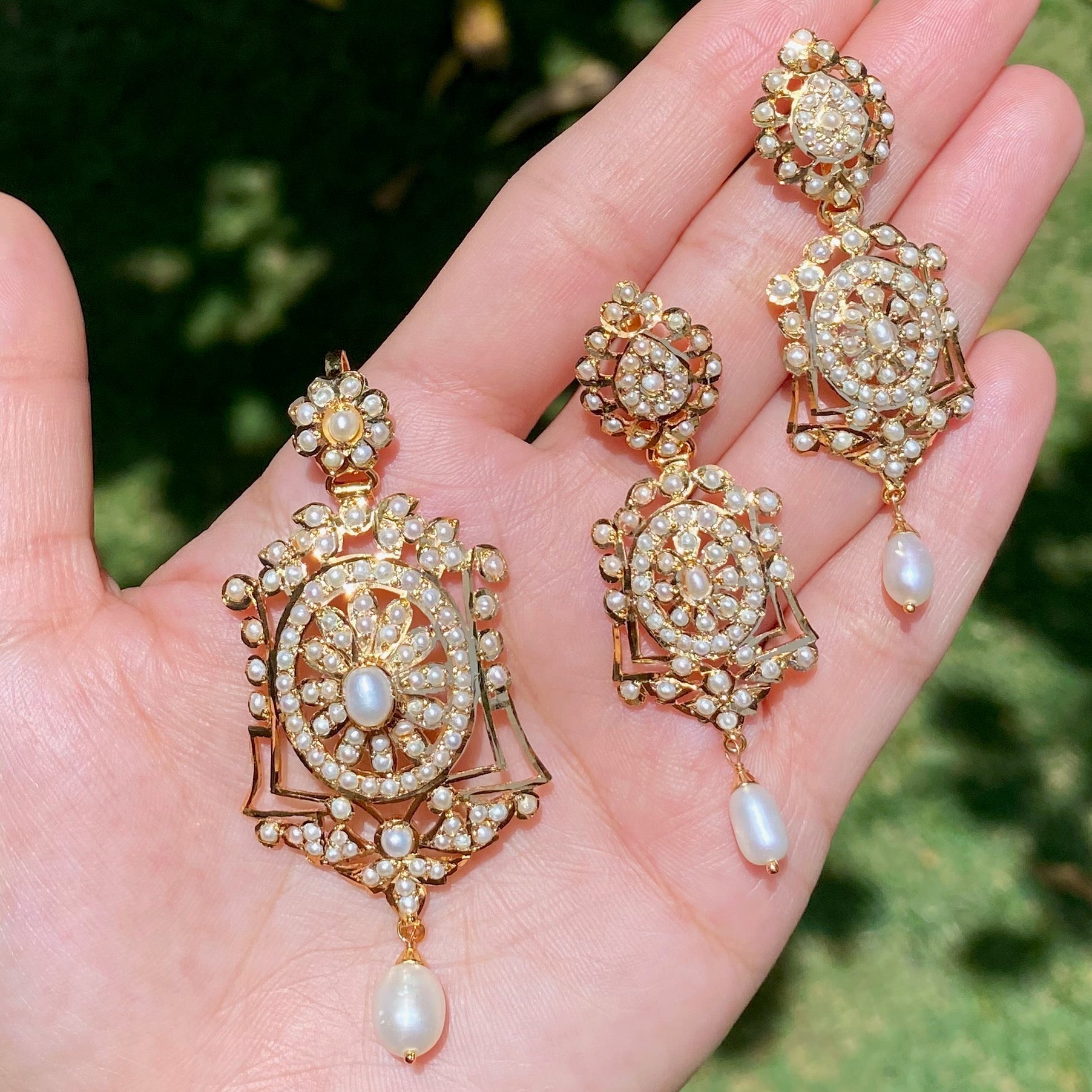Gold and pearl earrings held in a hand with a blurred green background